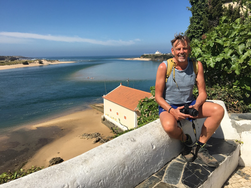Man zittend op muurtje met zee op de achtergrond op de rota vicentina in Portugal.
