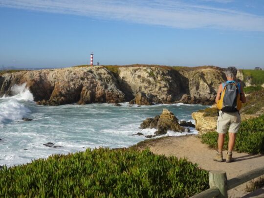 wandelaar langs kliffenkust met uitzicht op vuurtoren in Portugal