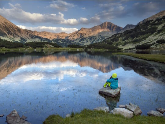 persoon zittend op steen bij een bergmeer in Bulgarije